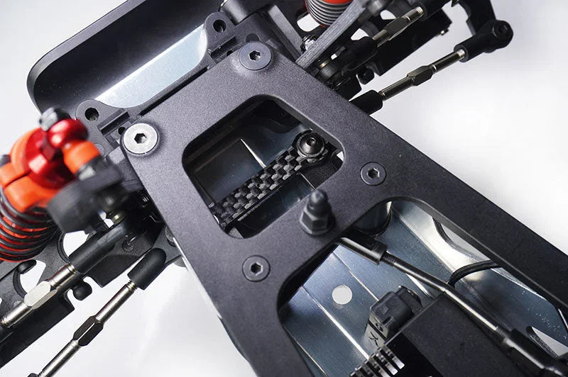 Close-up of RC car chassis showing carbon fiber center belt, metal suspension and shock absorbers