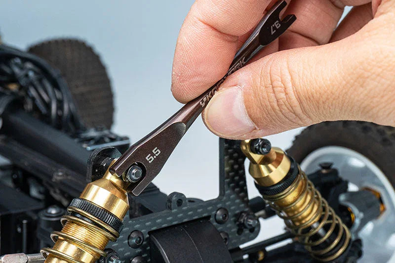 Hand using RC multi wrench tool adjusting gold shock absorber on RC car suspension