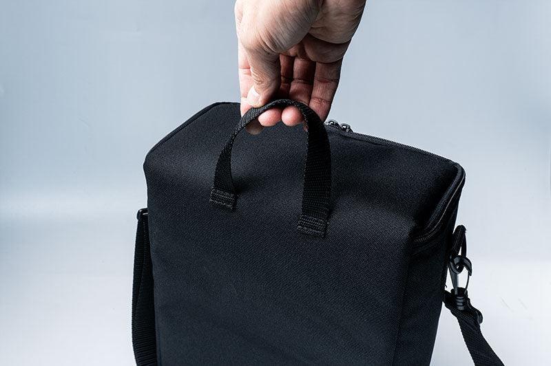 Hand holding black RC accessory pit bag with carrying handle and shoulder strap
