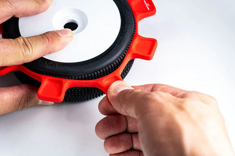 Hands using a red RC tire mounting tool on a black rubber RC car tire