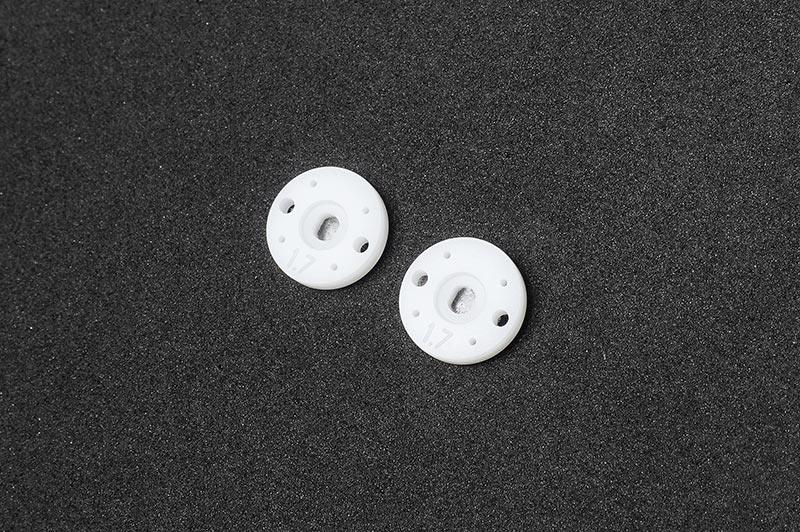 Pair of white RC shock pistons with multiple holes on black foam background