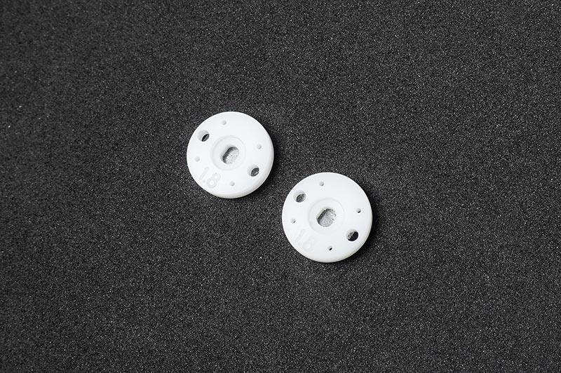 Pair of white RC shock pistons with multiple holes on black foam background