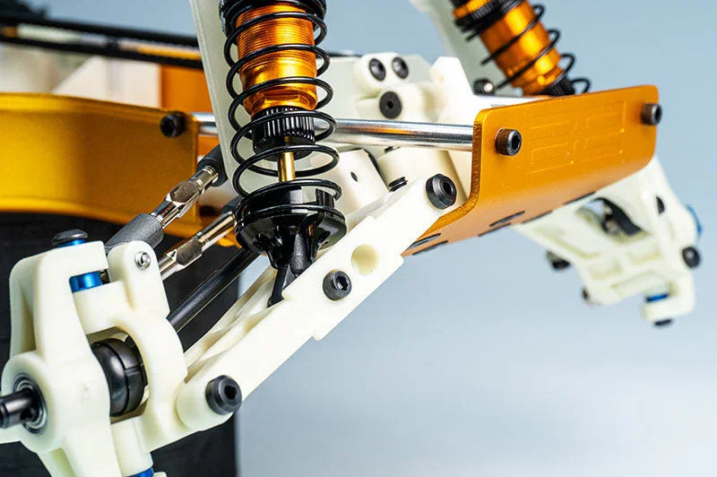 Close-up of RC car suspension system with orange shock absorbers and white chassis parts