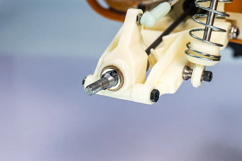 Close-up of RC car suspension arm, metal spring, and wheel axle assembly.