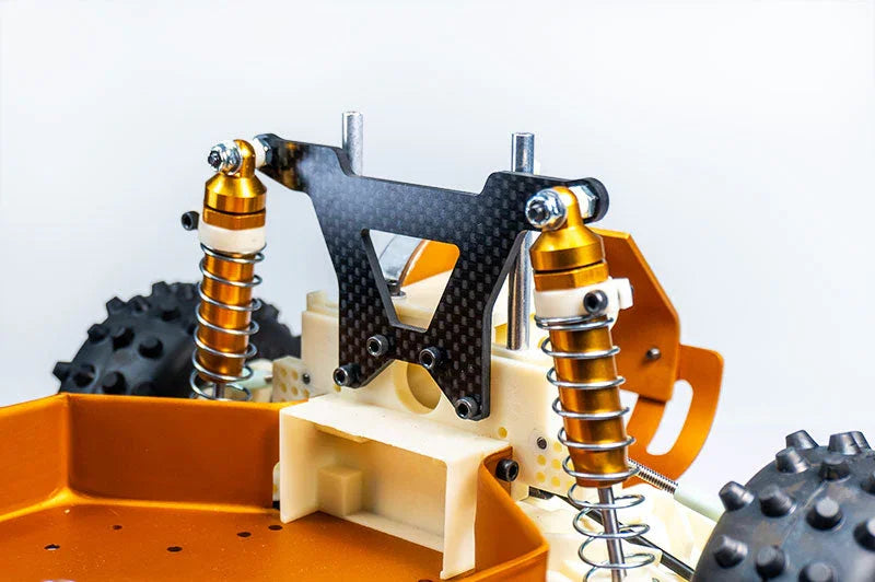 Close-up of RC car suspension with gold shocks, carbon fiber shock tower, and spiked wheels