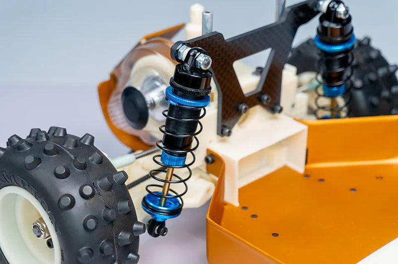 Close-up of RC car rear suspension, shocks, and knobby tire with orange chassis.