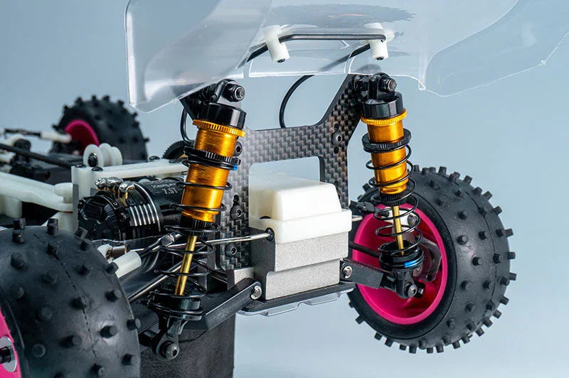 Close-up of RC car rear suspension with gold shock absorbers, knobby tires, and carbon fiber plate