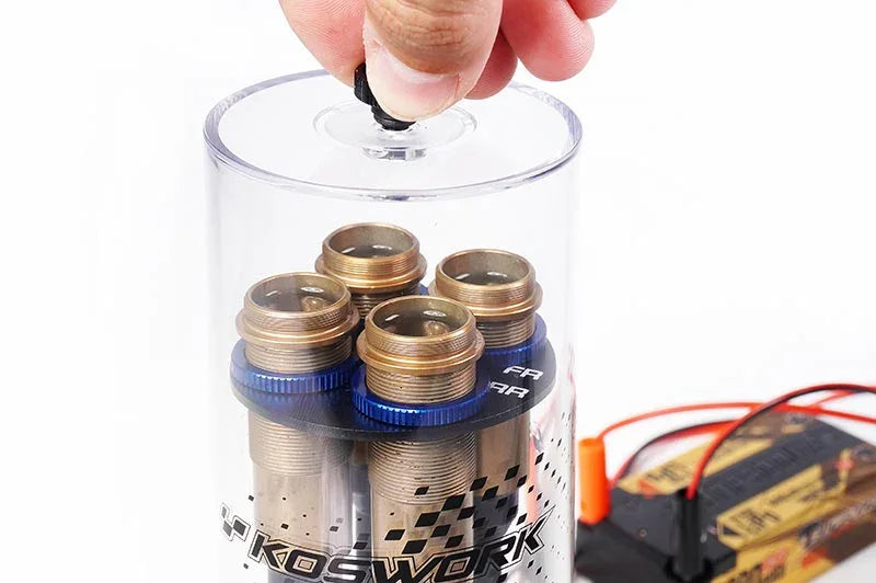 Hand opening clear case holding four RC shock absorbers with blue collars, RC battery nearby