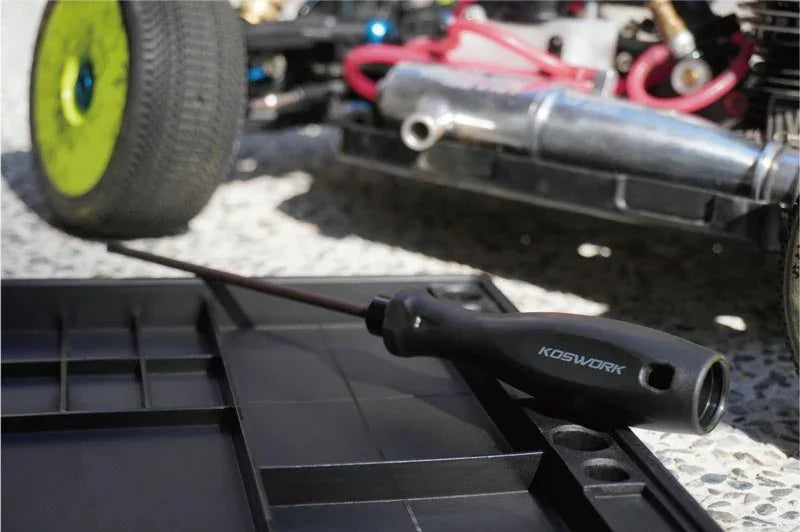 Koswork RC car tool with black handle next to RC pit mat and off-road vehicle outdoors.
