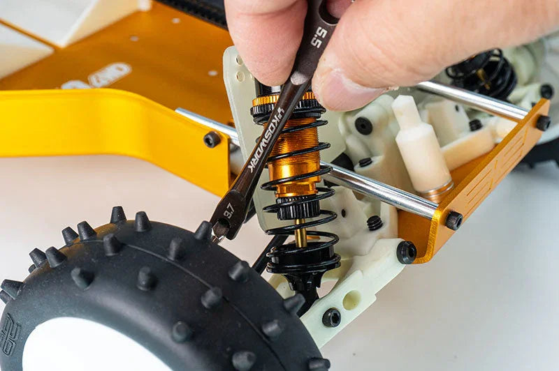 Hand using wrench to adjust RC car suspension shock near front wheel