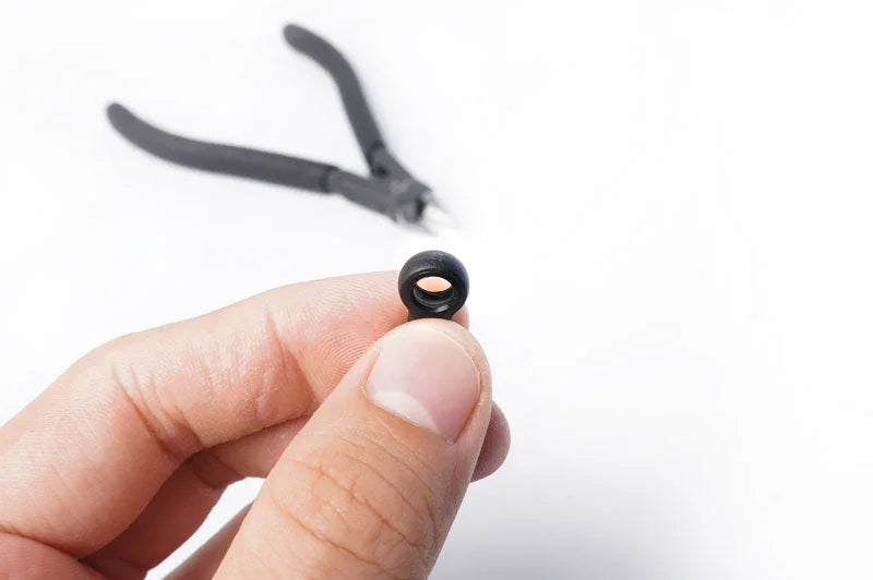 Koswork RC car accessory, small black rubber grommet, shown close-up with pliers