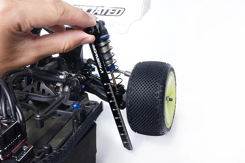 Hand measuring RC car shock absorber with a tuning tool next to off-road tire