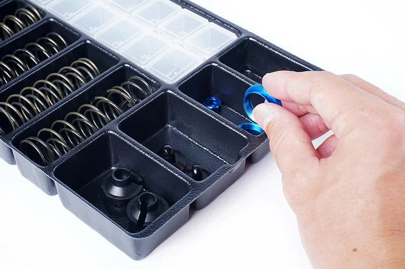 Hand selecting blue RC car part from organized pit box with springs and accessories.