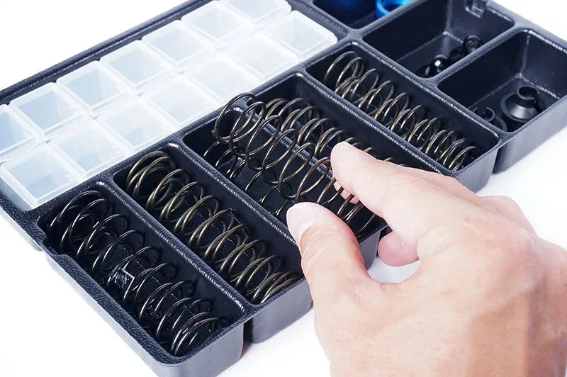 Hand picking RC car suspension spring from organized parts box, hobby accessories kit