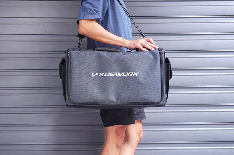 Person carrying a large black Koswork RC pit bag with shoulder strap in front of a gray garage door.