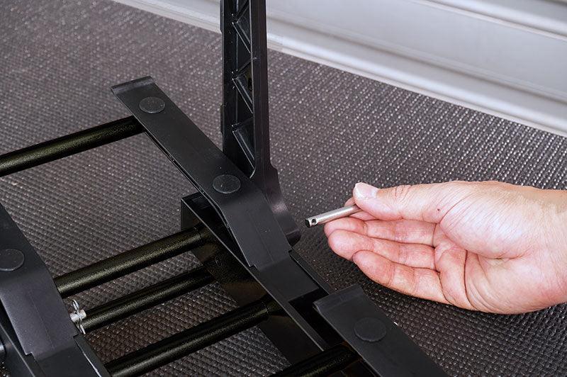 Hand assembling a black plastic RC car stand with metal rods on textured surface