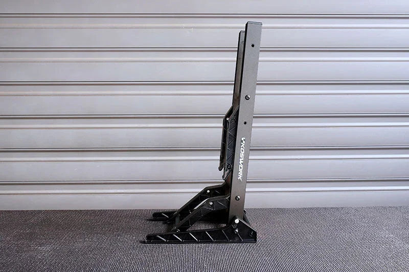 Black folding RC car stand with angled support, set on a textured surface