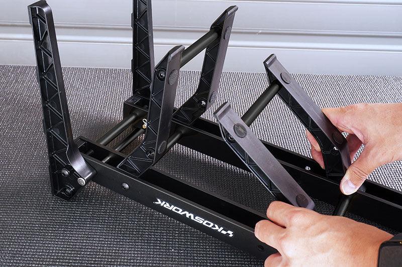 Person adjusting black RC car pit stand with foldable arms on textured surface