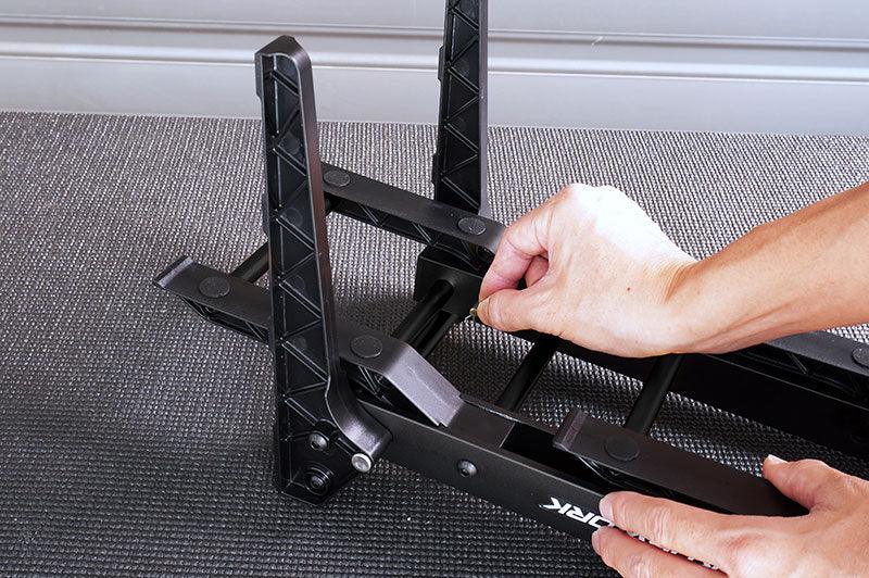 Hands assembling a black foldable RC car stand on a textured mat