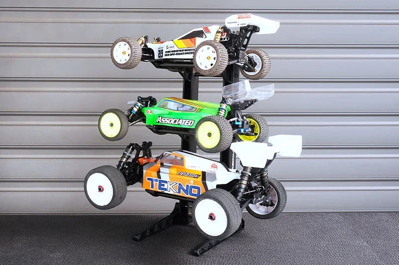 Three remote control cars displayed on a multi-tier RC car stand in a garage setting
