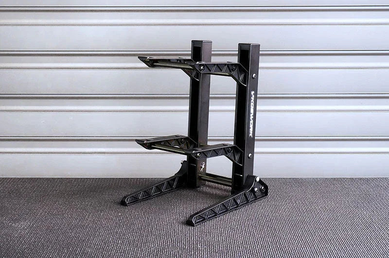 Black RC car stand with two tiers on a textured surface, garage setting