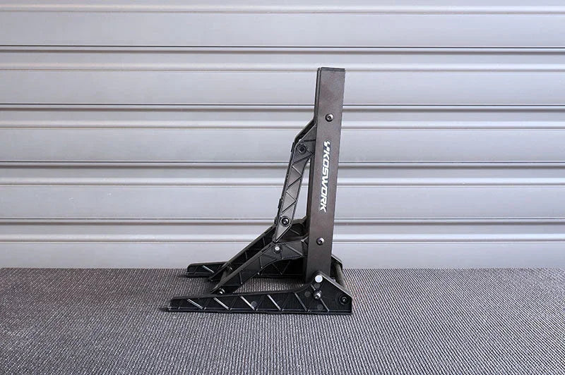 Black foldable RC car stand on textured surface against a gray panel wall