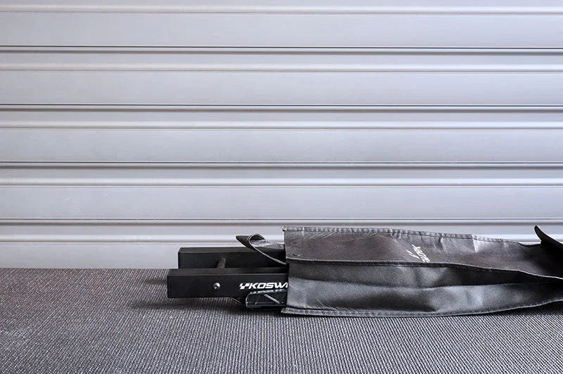 Black RC pit bag with visible handle, lying on grey carpet in front of panel wall