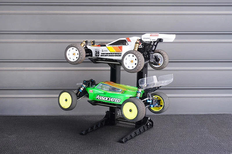 Dual tier RC car stand holding two 1/10 scale off-road buggy vehicles in a workshop setting